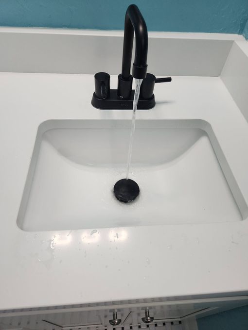 Black faucet running into a white bathroom sink with a black drain stopper.