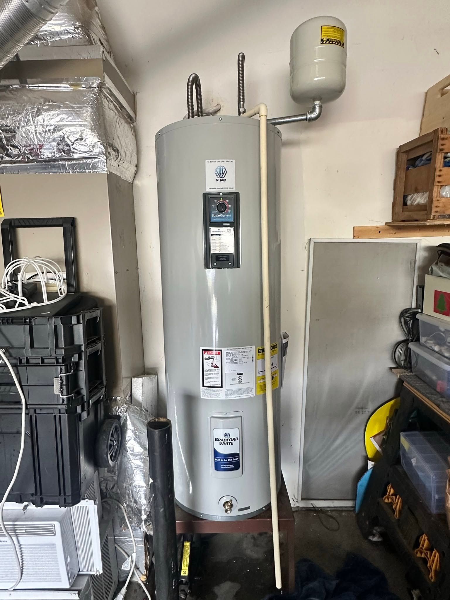 Water heater and expansion tank in a garage utility area with shelves and stored items.
