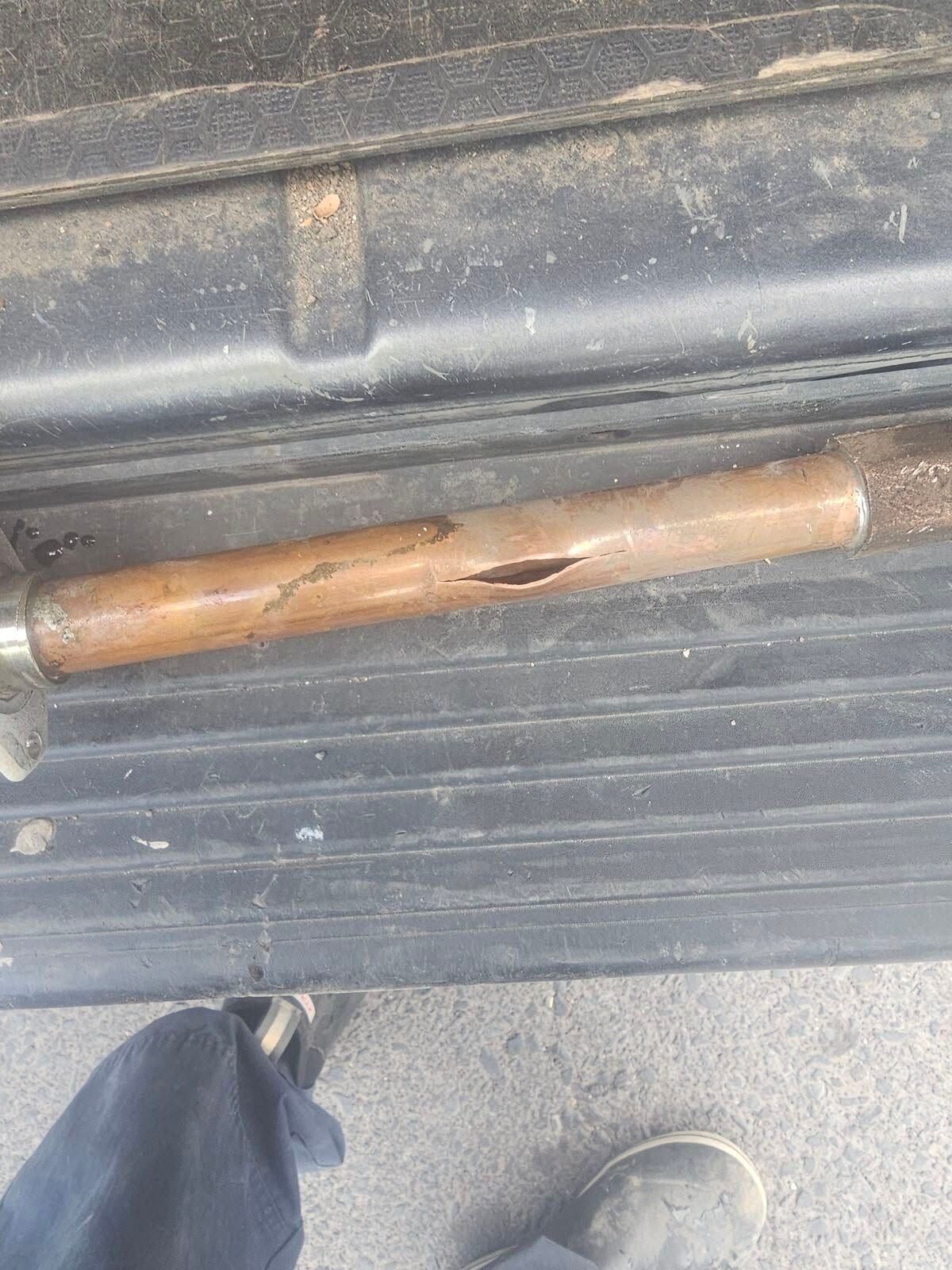 Broken wooden tool handle lying on a black textured surface beside a person's shoe.