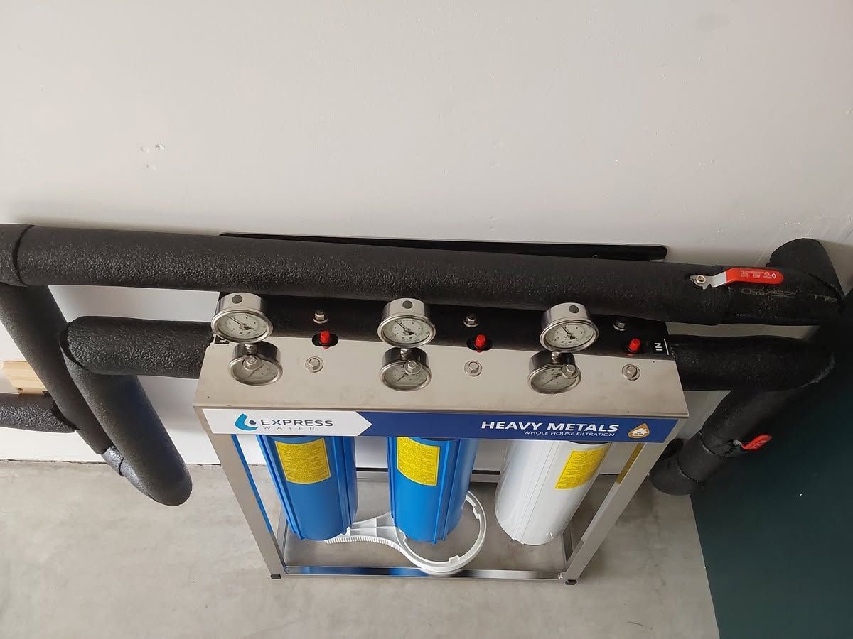 Wall-mounted water filter unit with blue and white canisters and black insulated pipes