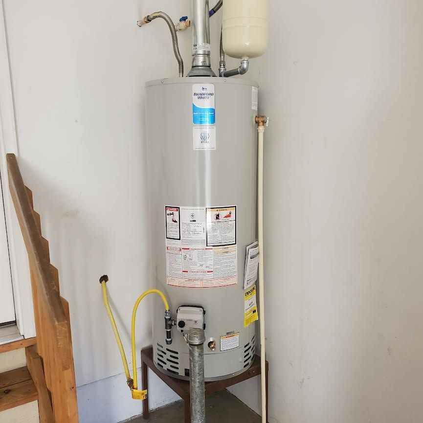 Water heater in a utility closet with pipes, a yellow gas line, and a white expansion tank.