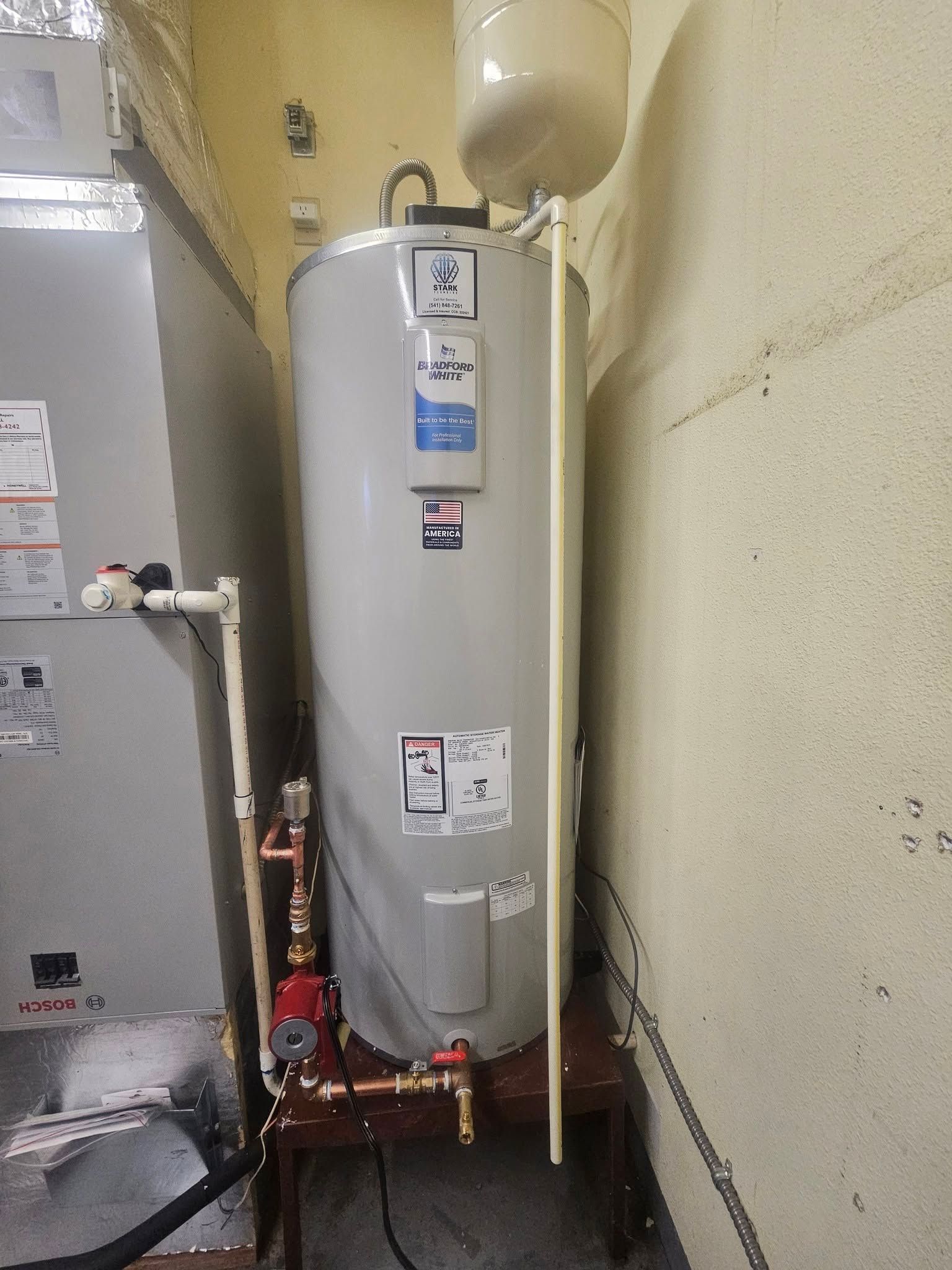 Water heater in a narrow utility alcove with plumbing, valves, and a nearby furnace.