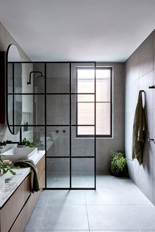 Modern bathroom with glass shower enclosure, floating wood vanity, and gray tiled walls and floor.