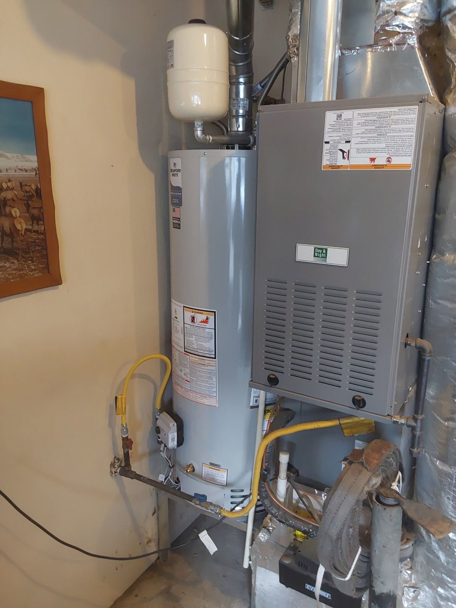 Residential water heater and furnace in a utility closet with pipes and venting.