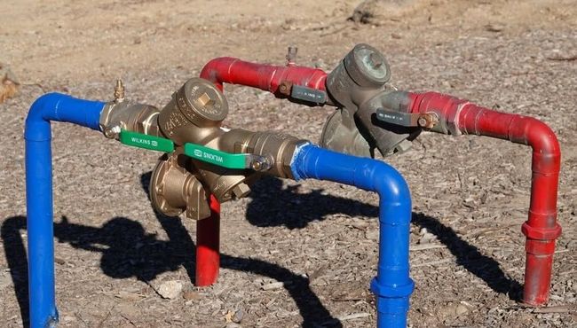 Colorful metal pipes and valves in a dirt area, with blue, red, and green sections.