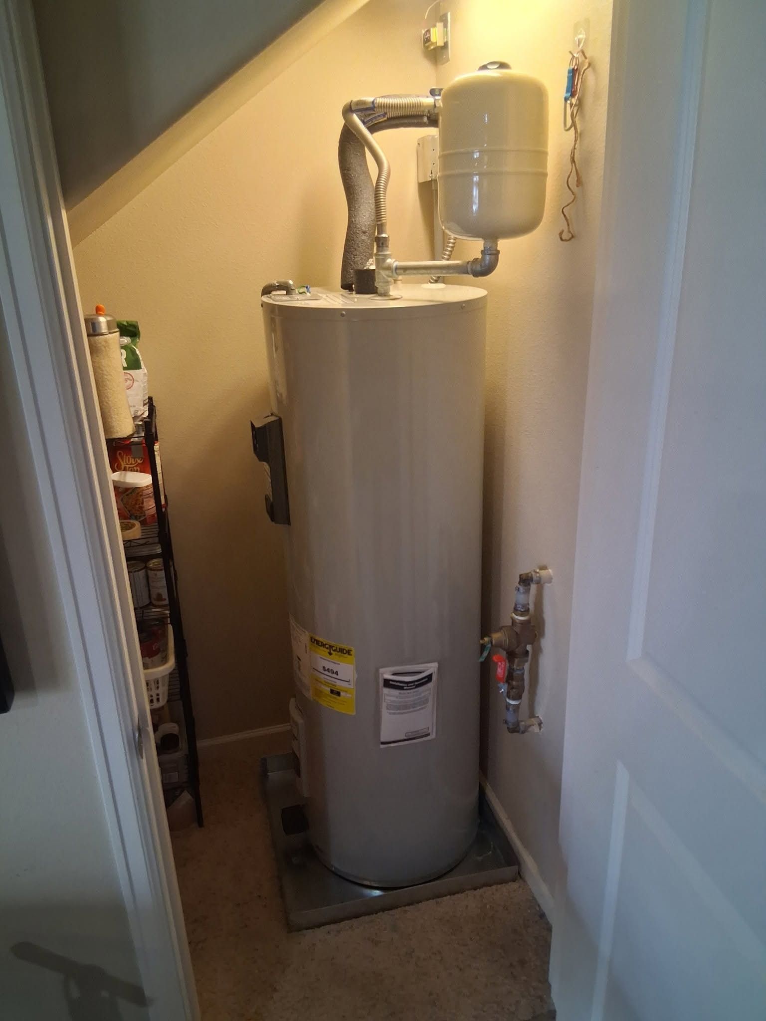 Tall beige water heater in a narrow utility closet under a staircase