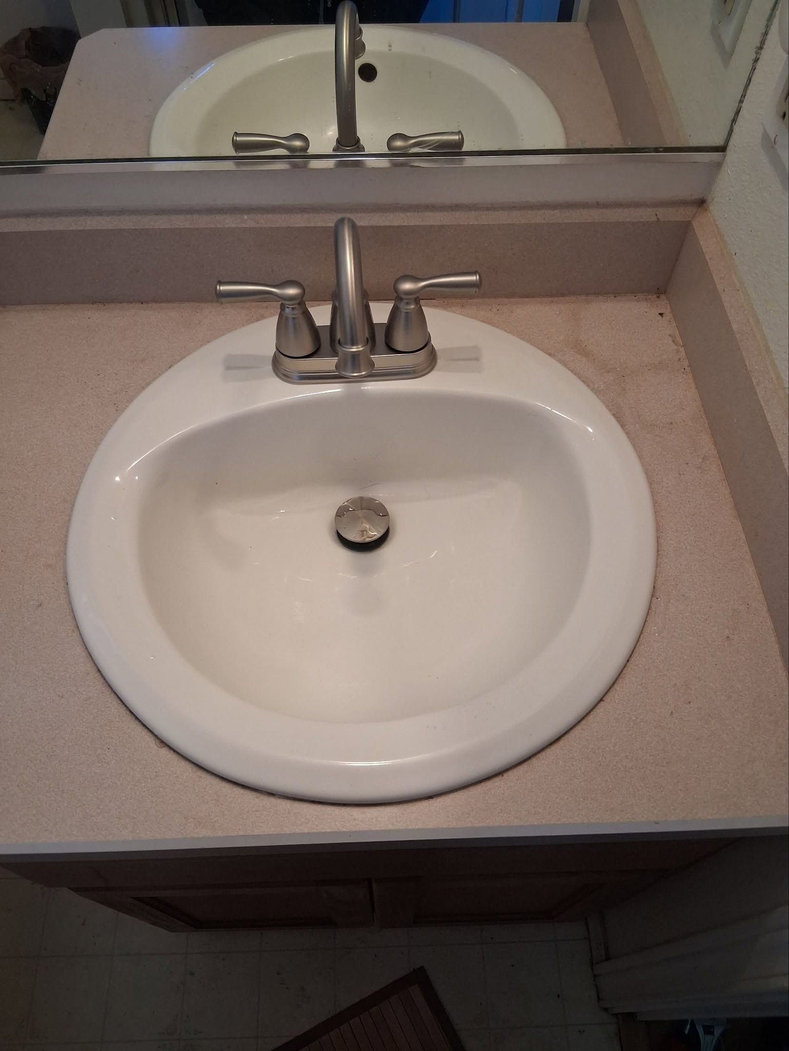 Bathroom sink with chrome faucet and mirror above, shown on a beige countertop.