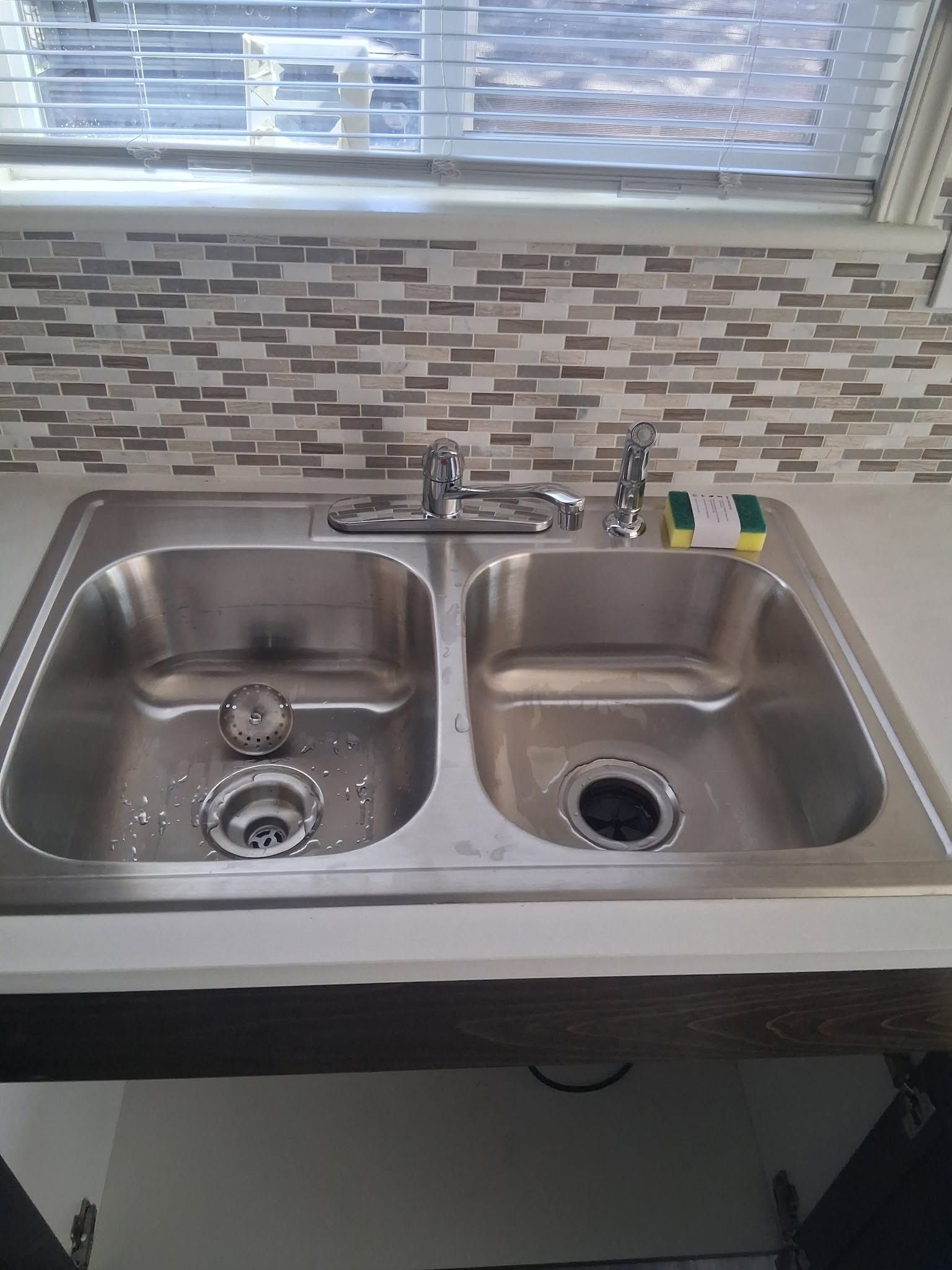 Kitchen double sink beneath a window, with a tile backsplash and dish soap on the counter.