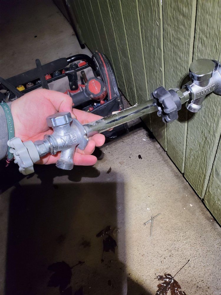 Hand holding a metal pipe fitting near a wall-mounted valve in a utility area