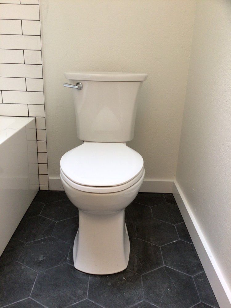 White toilet in a small bathroom with dark hex tile floor and light walls.