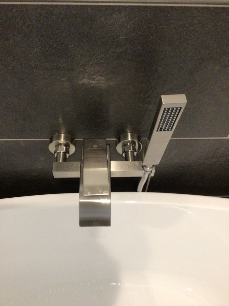 Modern bathtub faucet with handheld shower sprayer against dark tile wall