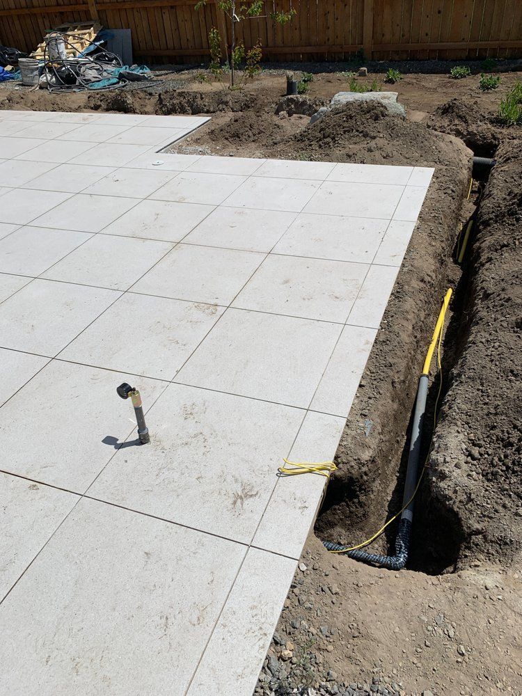 Outdoor tiled patio beside an excavation trench with exposed black pipe and construction debris