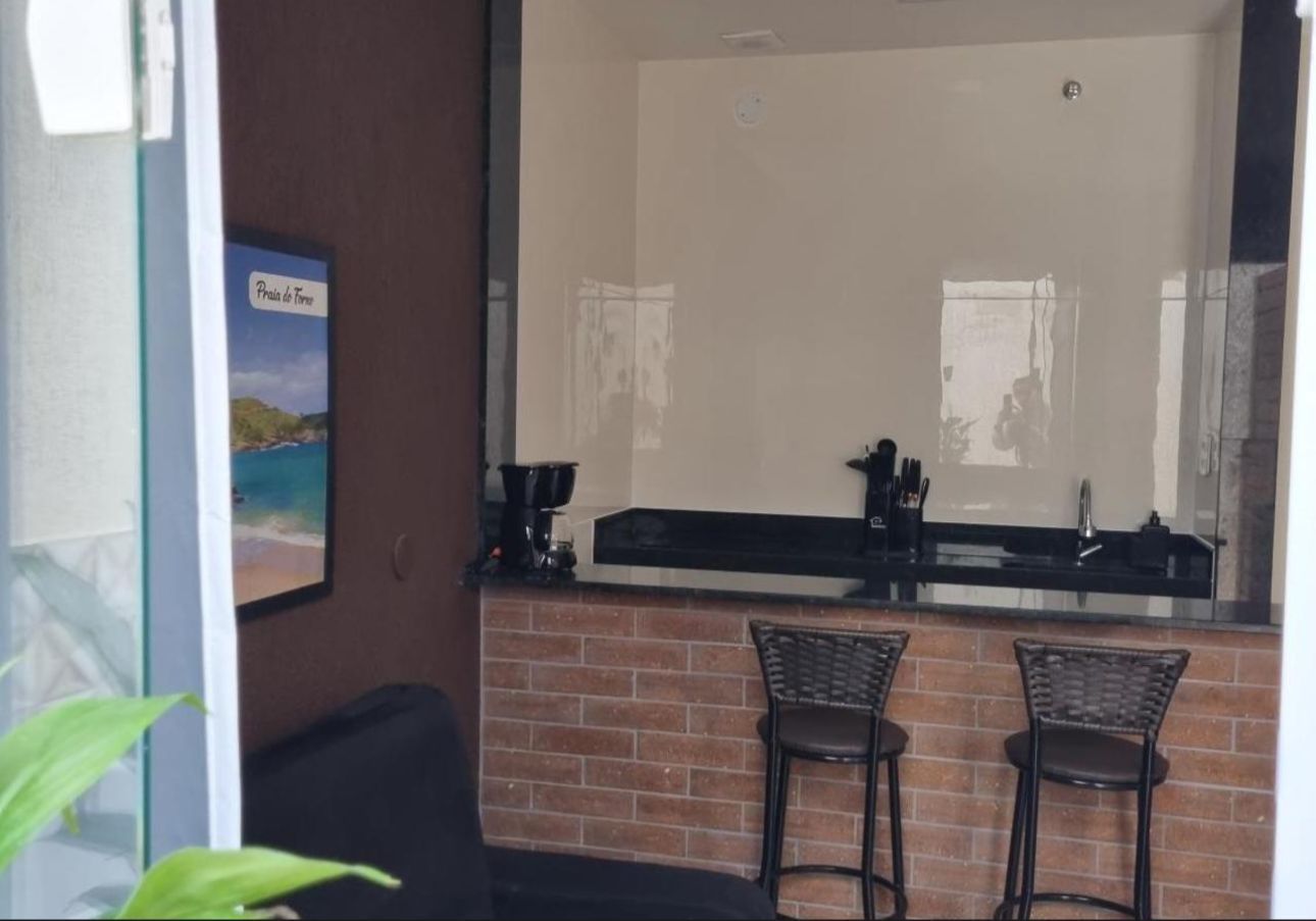 Pequeno bar residencial com dois bancos, fachada de tijolos e um grande espelho de parede em um interior pouco iluminado.