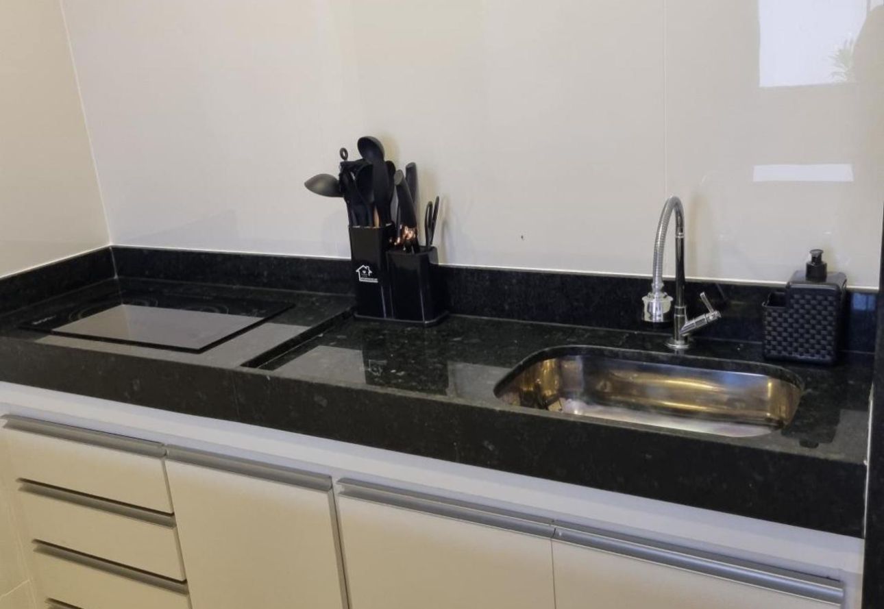 Bancada de cozinha com pia, torneira, porta-facas e fogão contra uma parede branca.