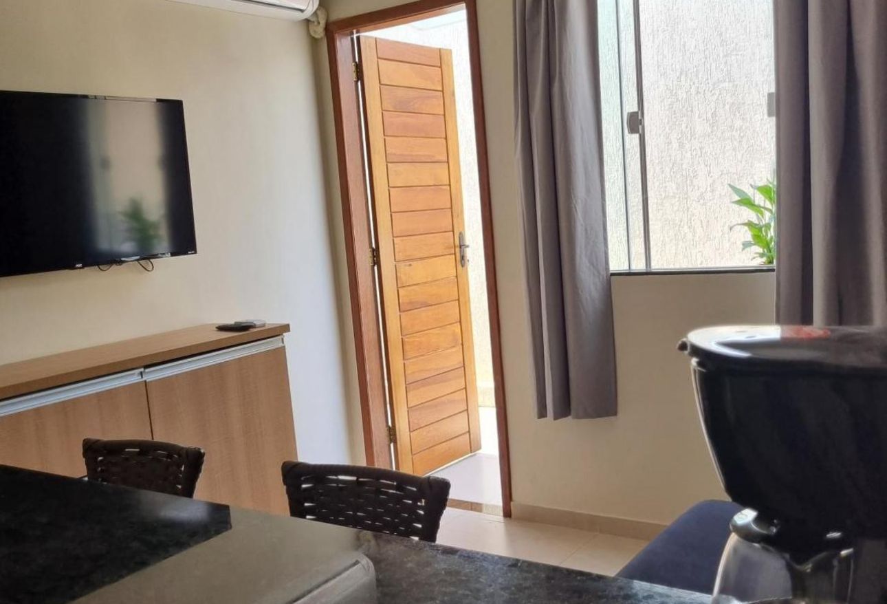 Sala de estar moderna com TV de parede, sofá, mesa de jantar e porta de madeira aberta para a varanda.