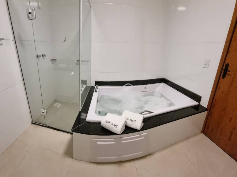 Banheiro moderno com box de vidro, banheira de canto e toalha na borda da banheira.