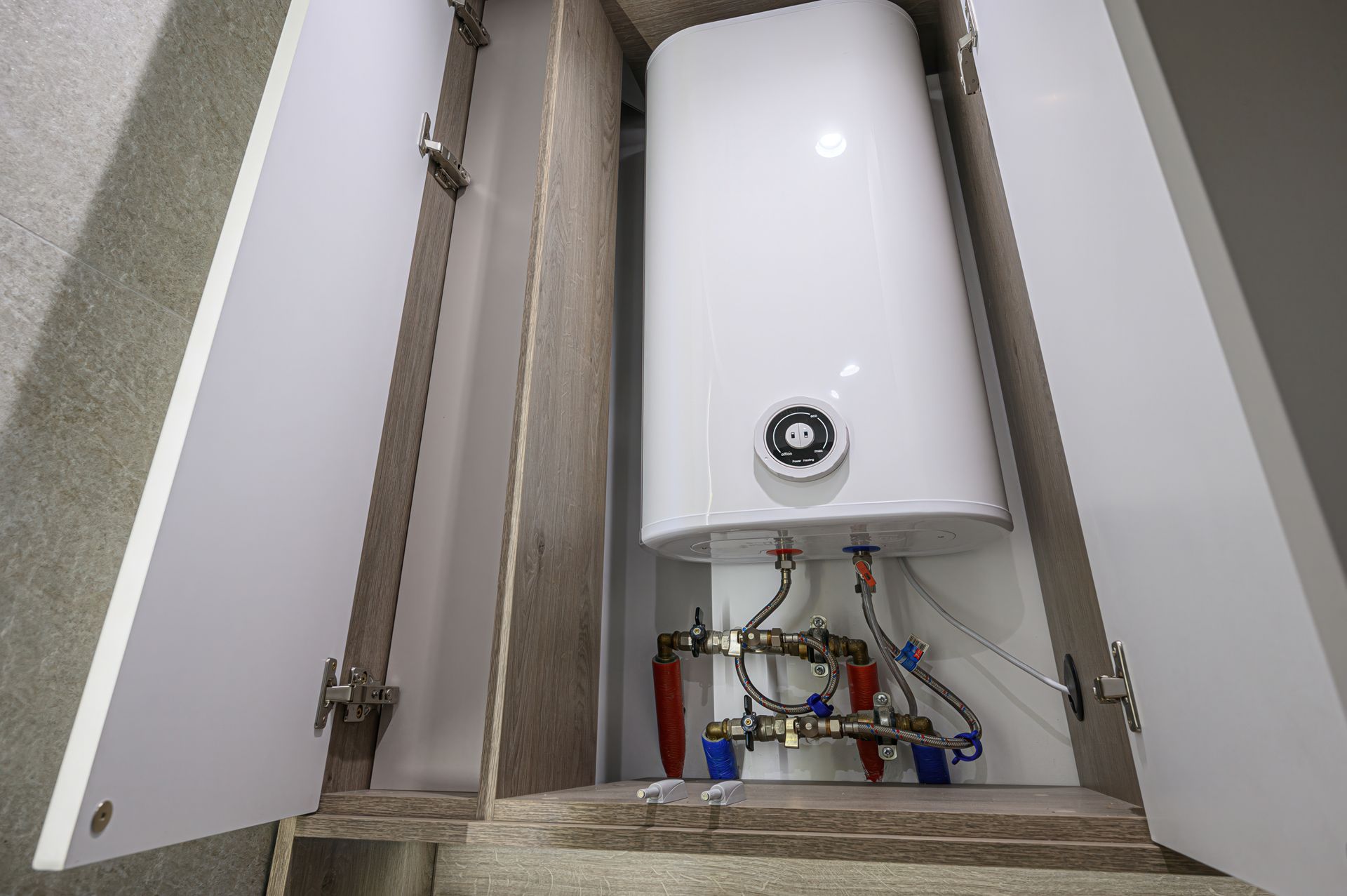White water heater with exposed pipes in a narrow utility closet