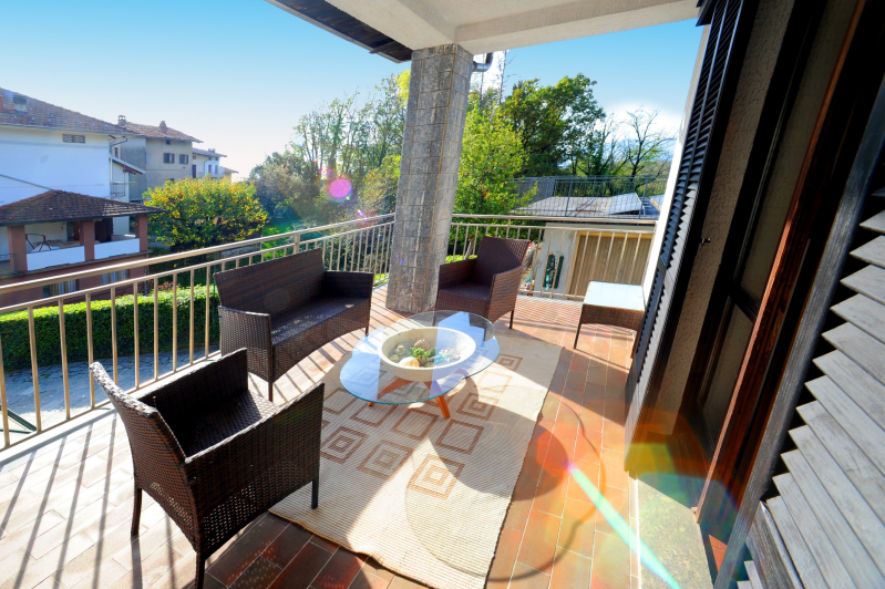 Balcone con mobili in vimini, tappeto e vista sugli edifici e sul verde.
