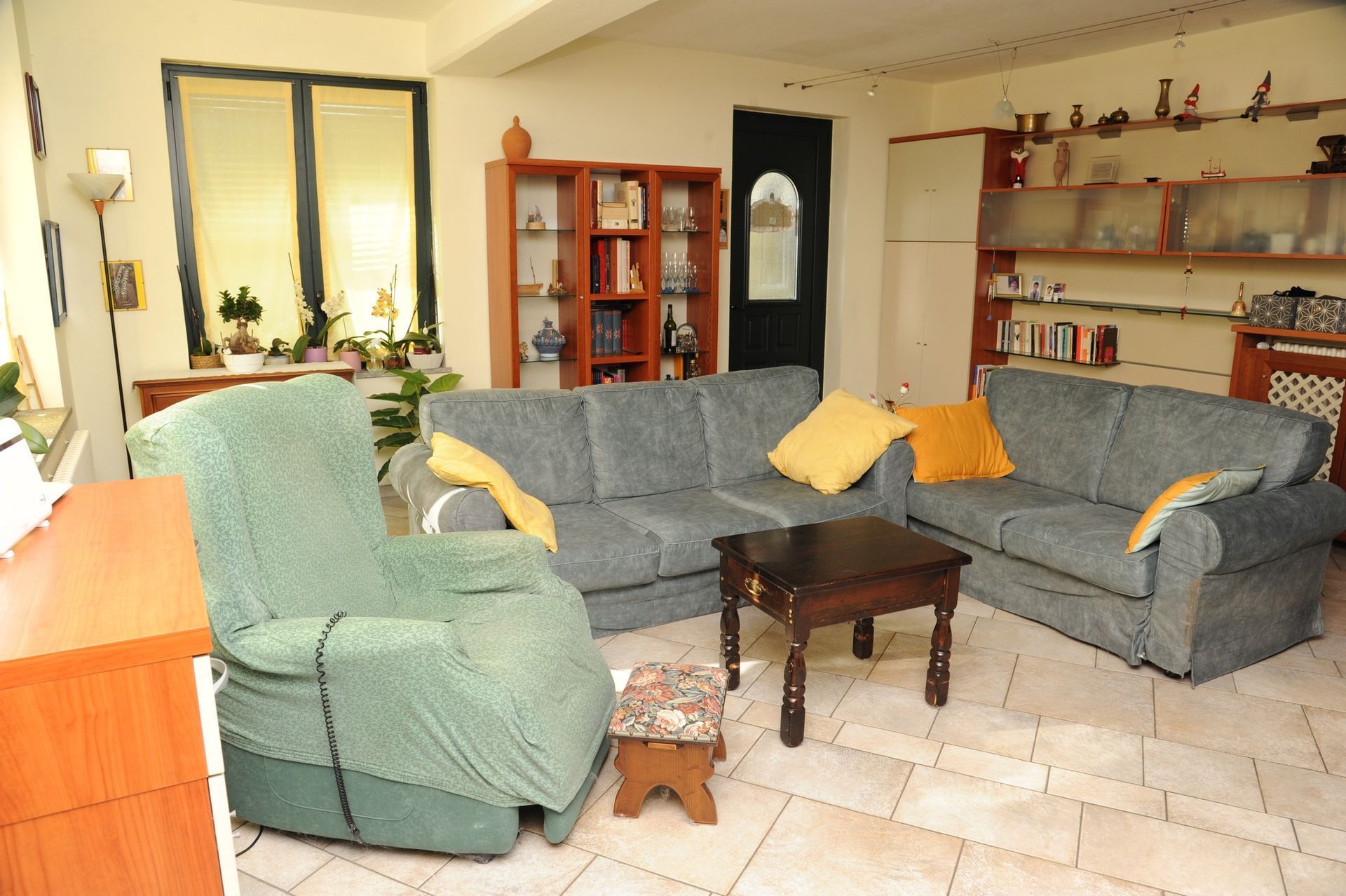 Soggiorno con divani blu, poltrona verde, tavolo in legno e mensole decorative.