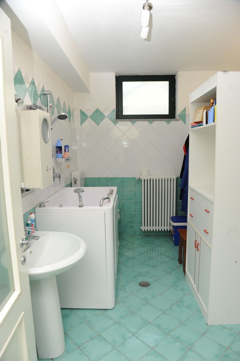 Bagno con sanitari bianchi, pavimento verde acqua e piastrelle a rombi.