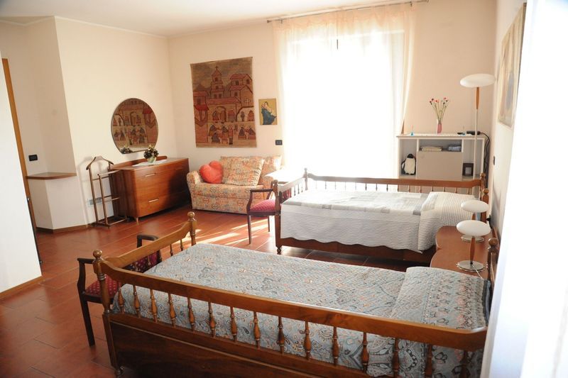 Camera da letto con due letti singoli, mobili in legno, opere d'arte e una finestra con tende trasparenti.