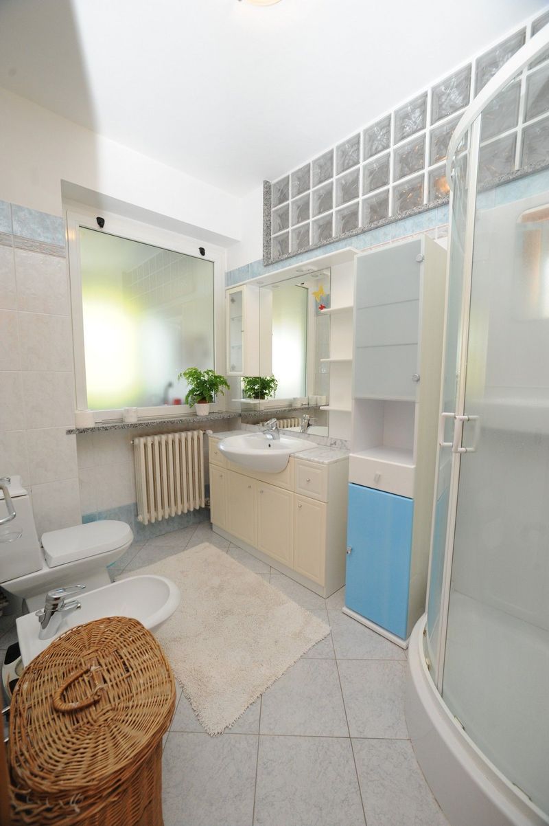 Bagno con WC, lavandino, doccia e cesto di vimini. Colori azzurro e beige.