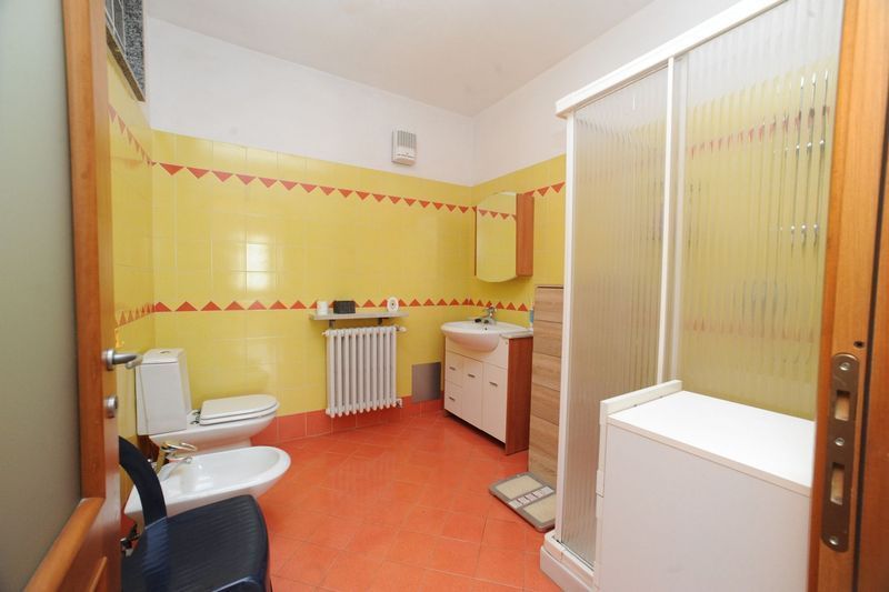 Bagno con pareti gialle, pavimento rosso, WC, bidet, box doccia e mobile lavabo.