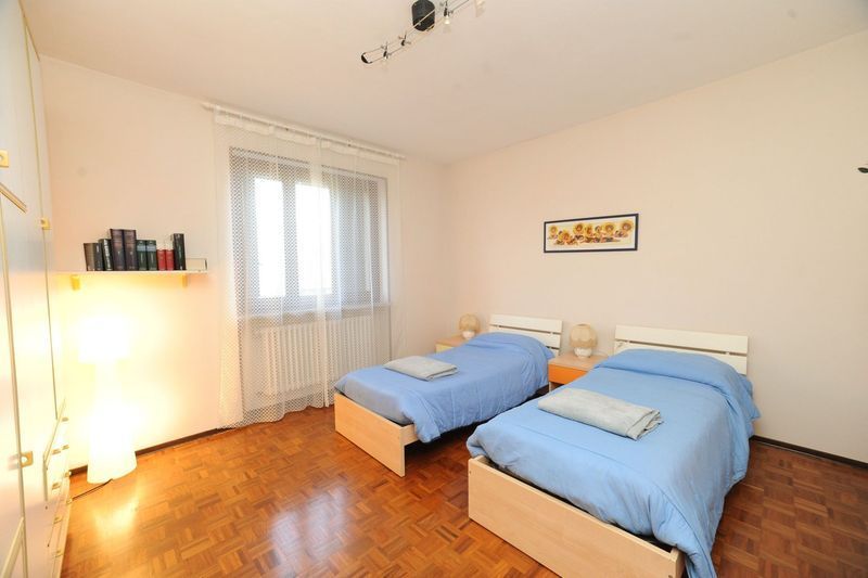 Due letti con lenzuola blu in una camera da letto luminosa con finestra, pavimento in legno e un piccolo quadro.