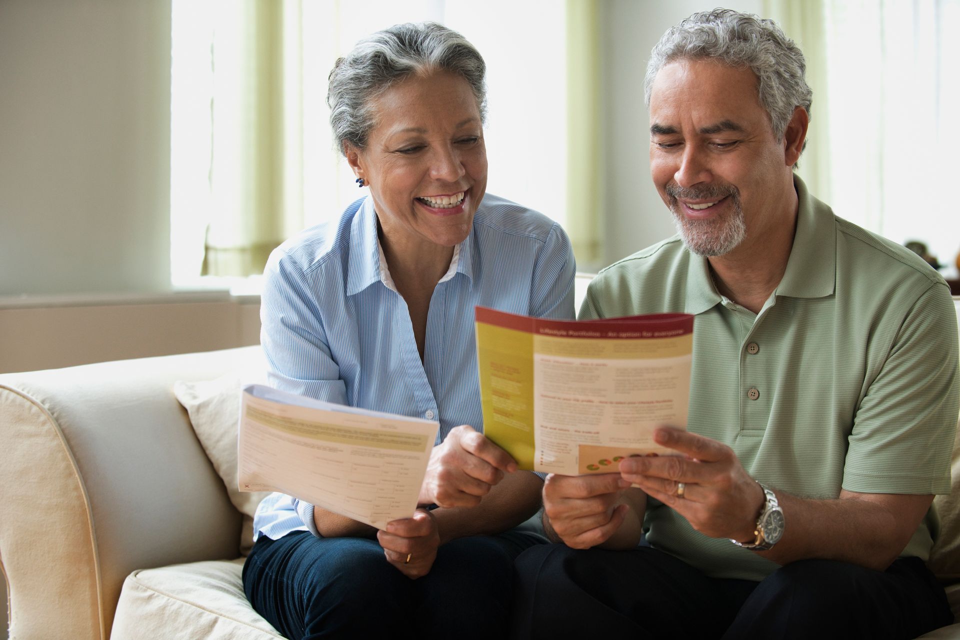 A man and a woman are sitting on a couch reading a book.