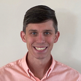 Smiling man in a light pink shirt against a plain background