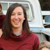 Smiling woman in a burgundy top standing in front of a white vintage truck