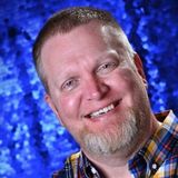 Smiling man in plaid shirt against a blue studio backdrop