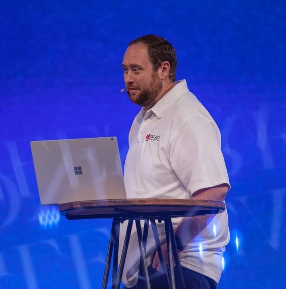 Man speaking at a podium with a laptop on a blue-lit stage