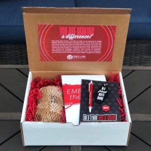 Open gift box with red tissue, a card, and a black shirt inside.