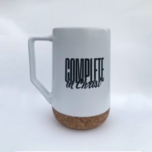 White mug with cork base and handle, printed with “complete in Christ” text in black.