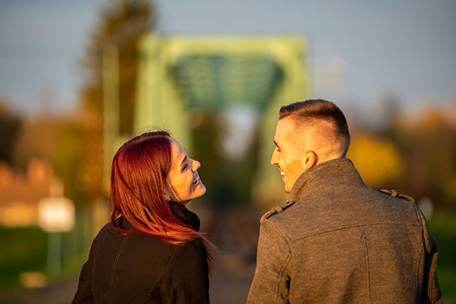 Two people walking outdoors at sunset, looking at each other on a blurred bridge.