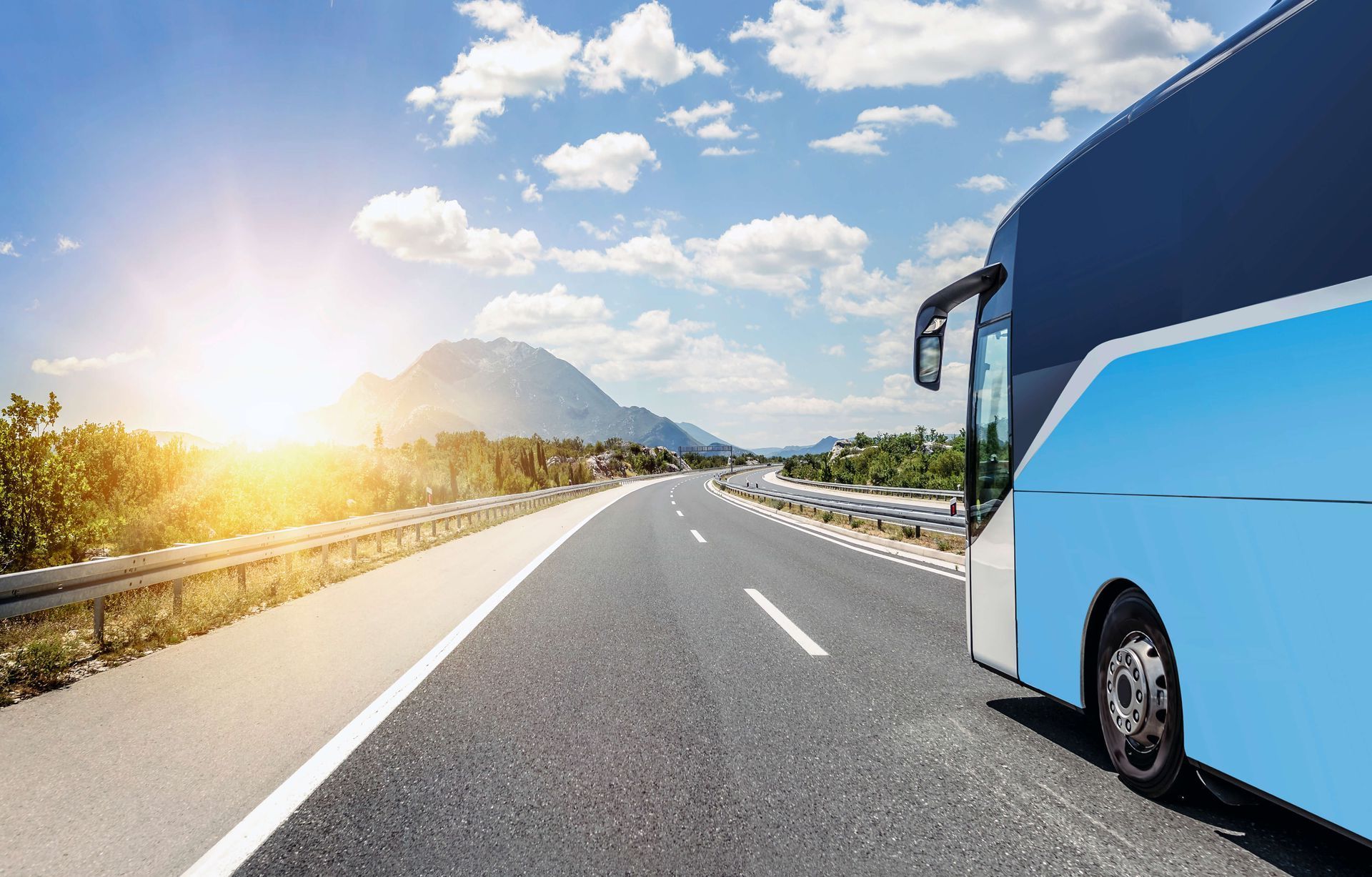 Blue bus driving on a sunny highway with mountains in the distance