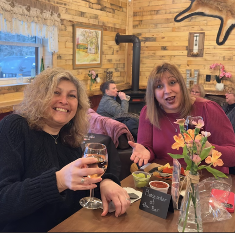 Two women sitting at a table with a sign that says 
