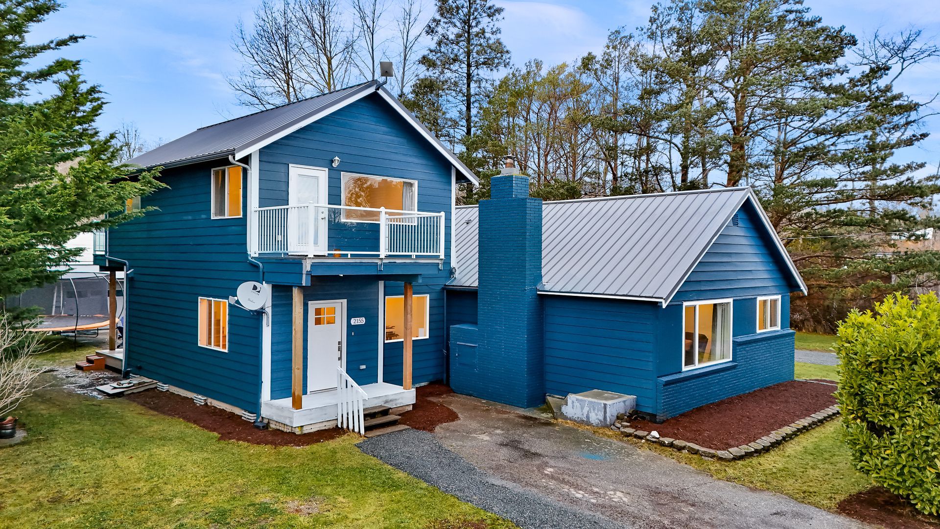 Exterior of 2155 Postal Avenue with blue siding, metal roof, and balcony.
