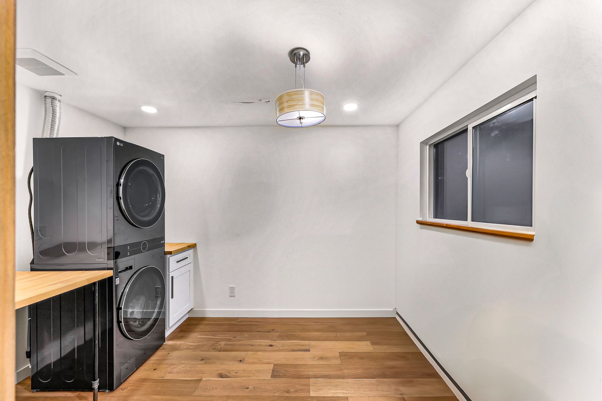 Laundry room with stackable washer and dryer, butcher block countertops, and recessed lighting.
