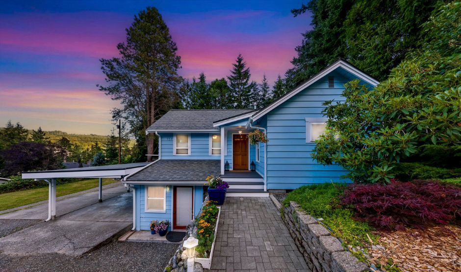 Blue Craftsman-style home with covered front porch, carport, landscaped entry, and colorful sunset sky.