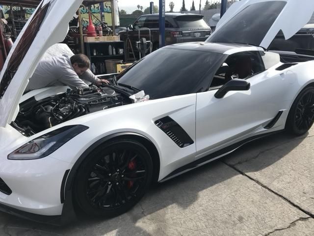 A man is working on the engine of a white sports car