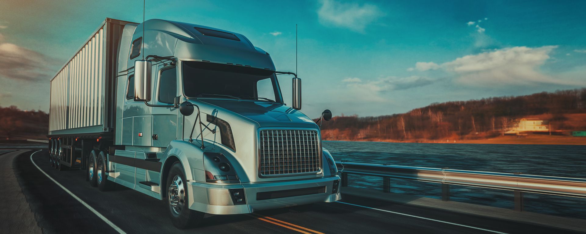 A semi truck is driving down a highway next to a body of water.