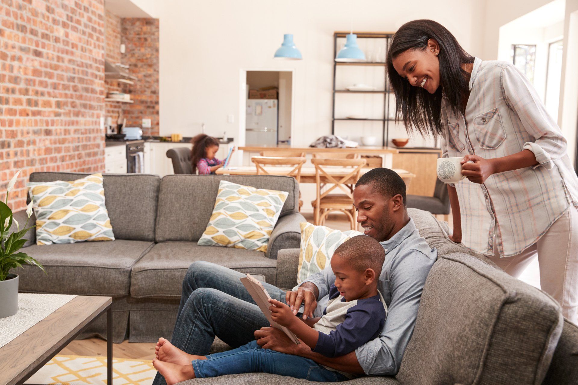 A family is sitting on a couch in a living room looking at a tablet.