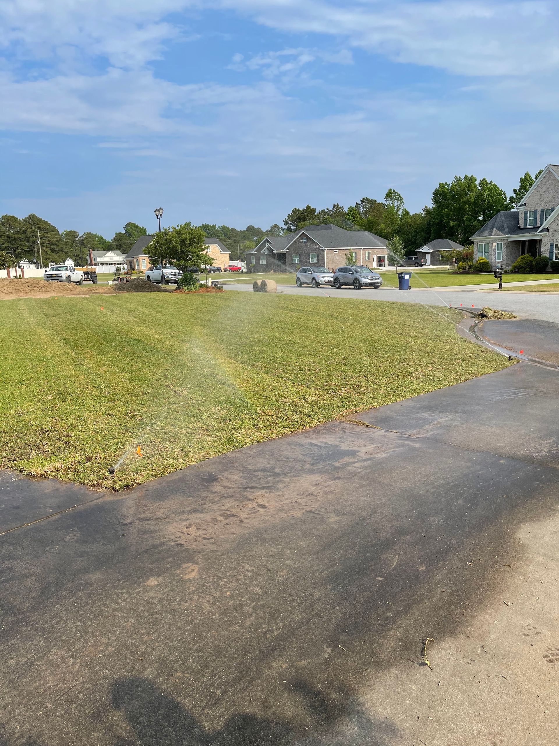 Green lawn with sprinkler system, houses in background, sunny day.