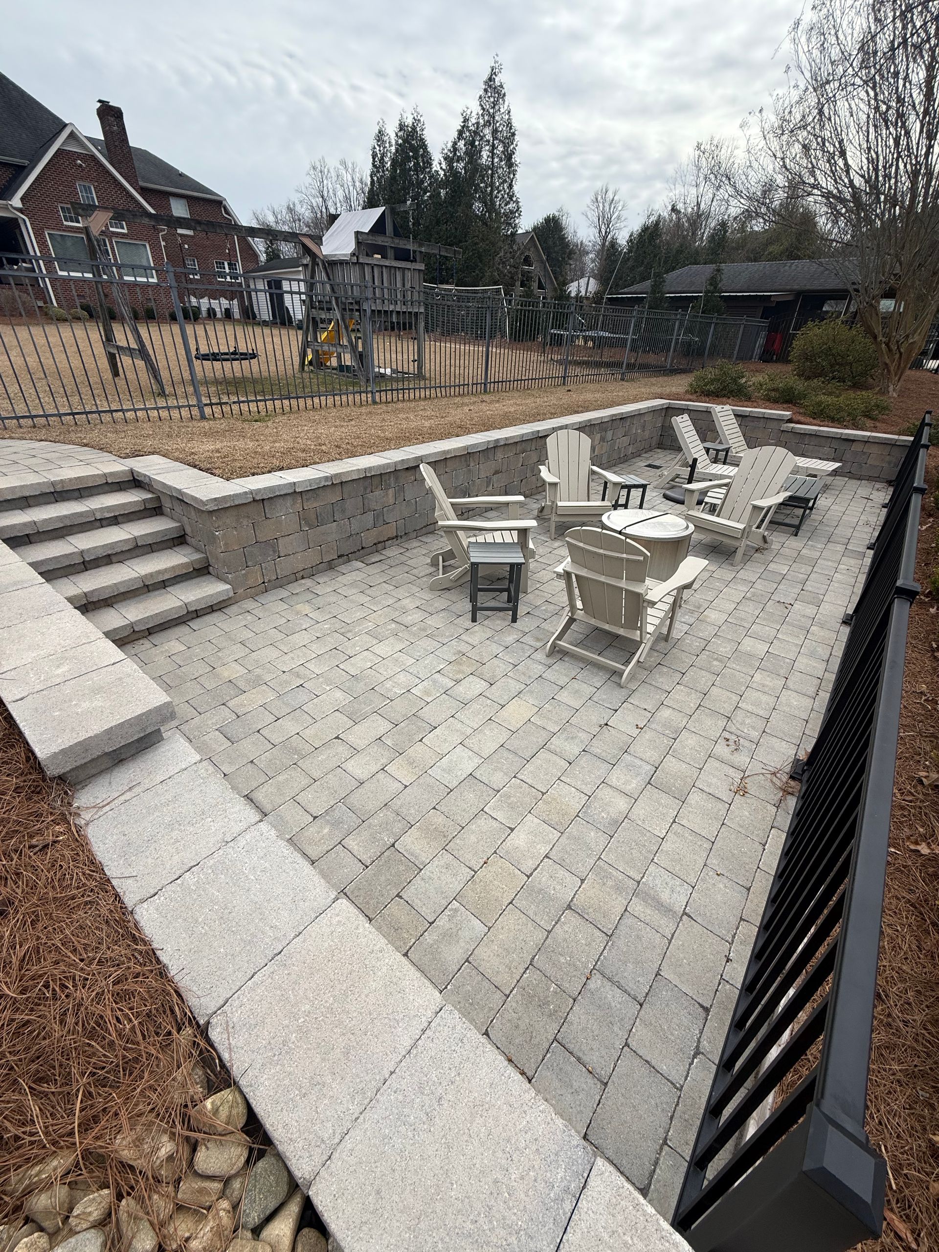 Stone patio with seating area, retaining wall, steps, and a wrought iron fence.
