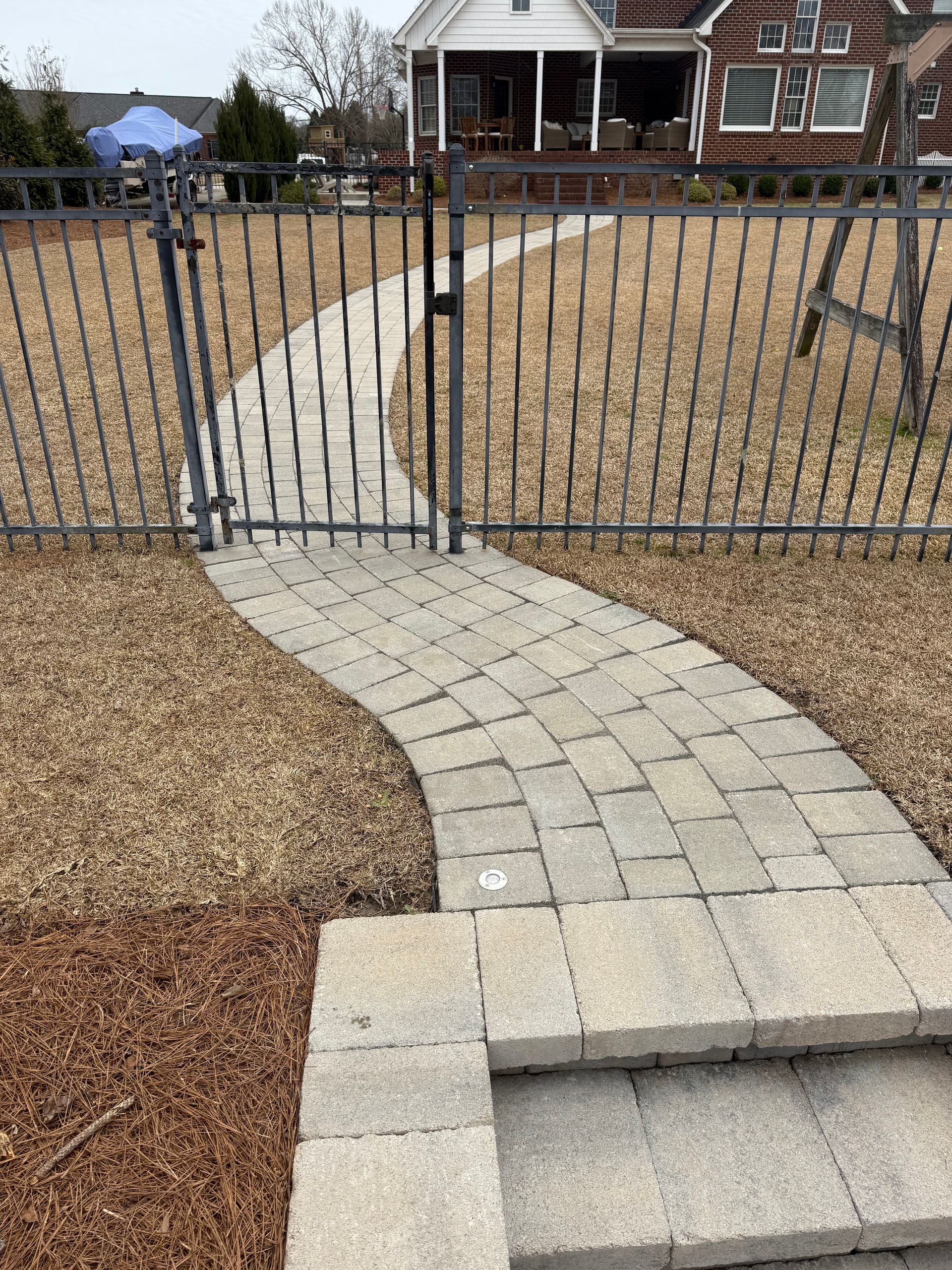 Stone path curves behind a black metal fence, leading to a house. Steps lead up to the path.