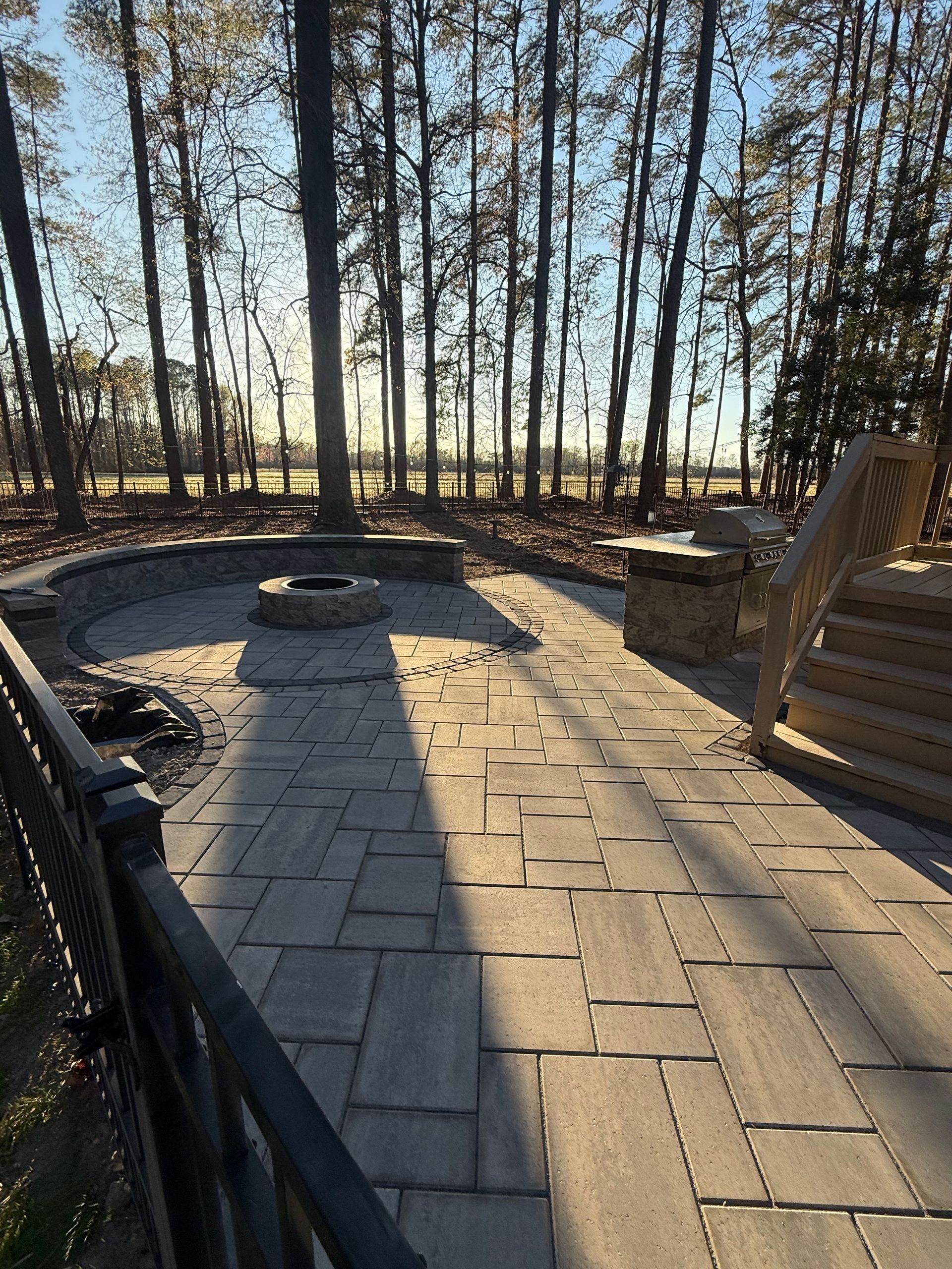 Stone patio with fire pit, surrounded by trees and a sunny landscape.