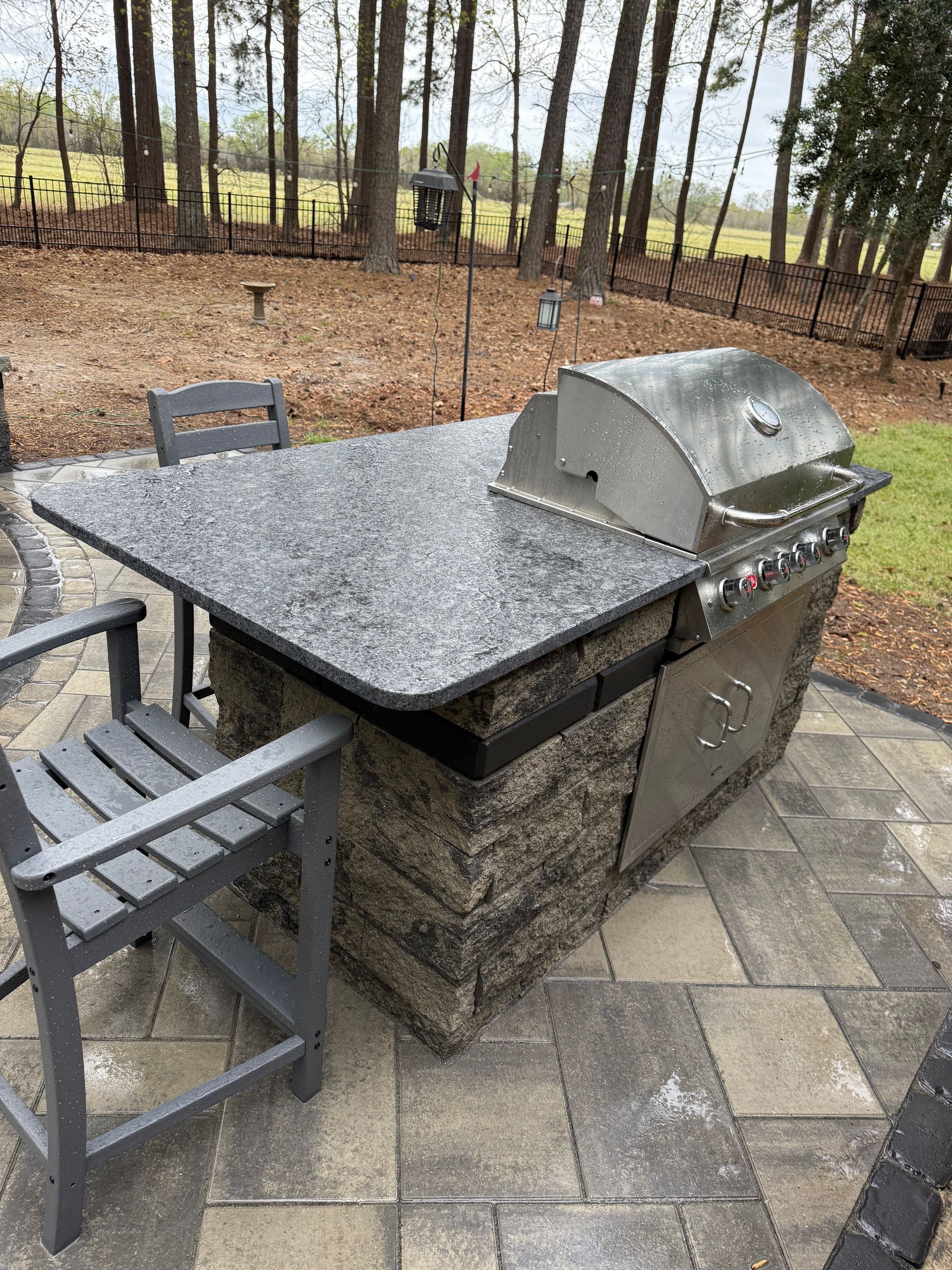 Outdoor kitchen with a granite countertop, grill, and seating on a patio.