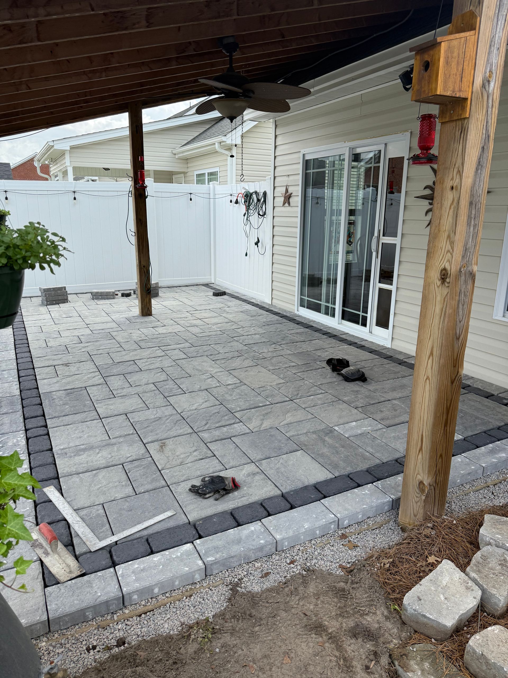 Patio with gray pavers, black border, wooden posts, and white fence.